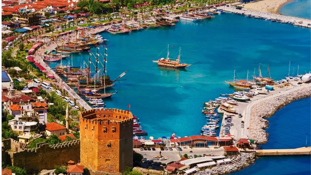 Wooden tour boat cruising past the medieval Red Tower and Seljuk Shipyard cliff in Alanya Turkey