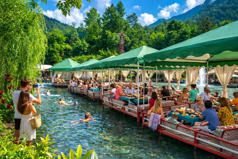Travelers dining on traditional wooden seating platforms over the flowing Dim River near Alanya