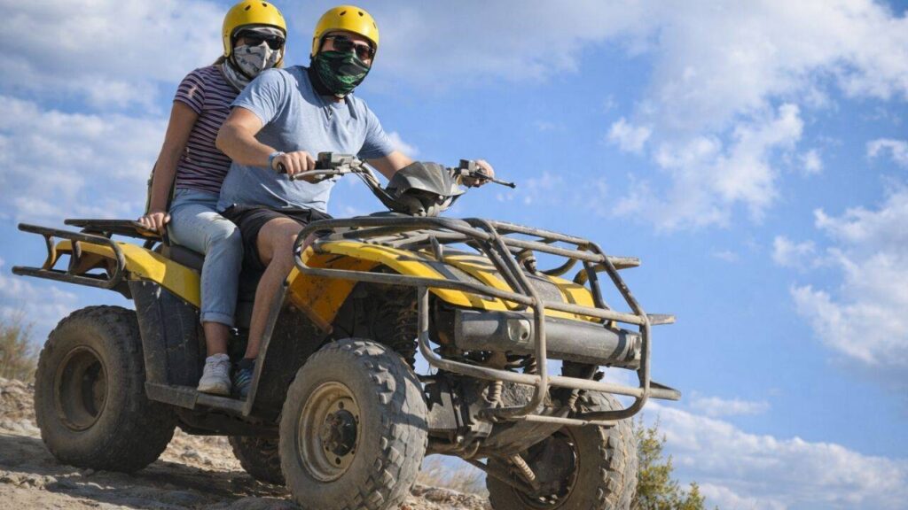 Couple wearing safety helmets riding a double quad bike on mountain dirt track in Side