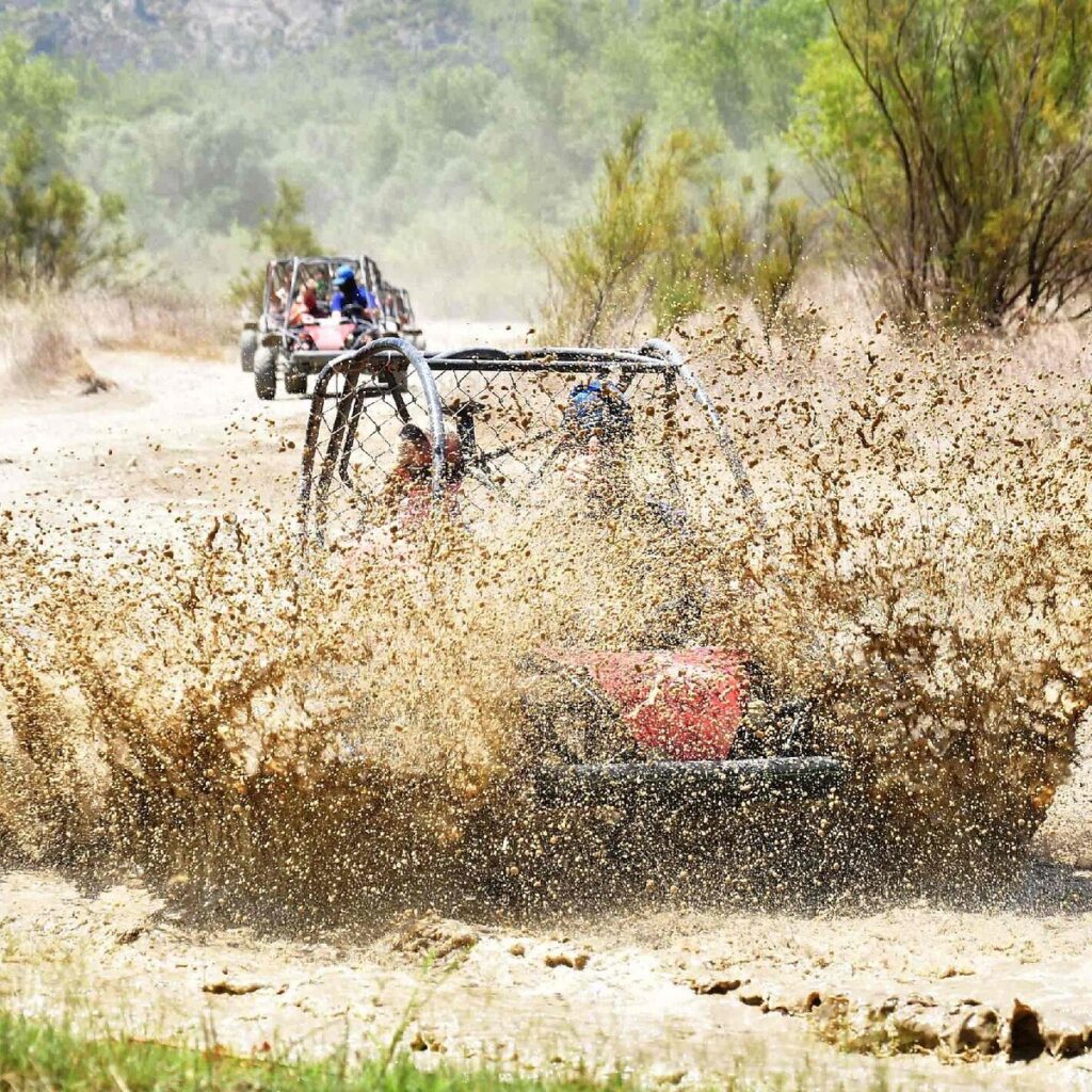 Convoy of buggies navigating a muddy dry riverbed trail on a Side Turkey off-road tour with hotel pickup included.