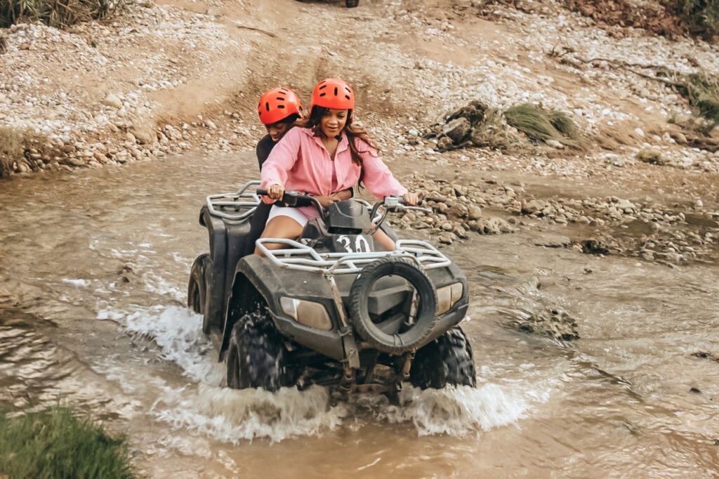 Quad bike splashing through mountain stream water pit during Side off-road safari tour