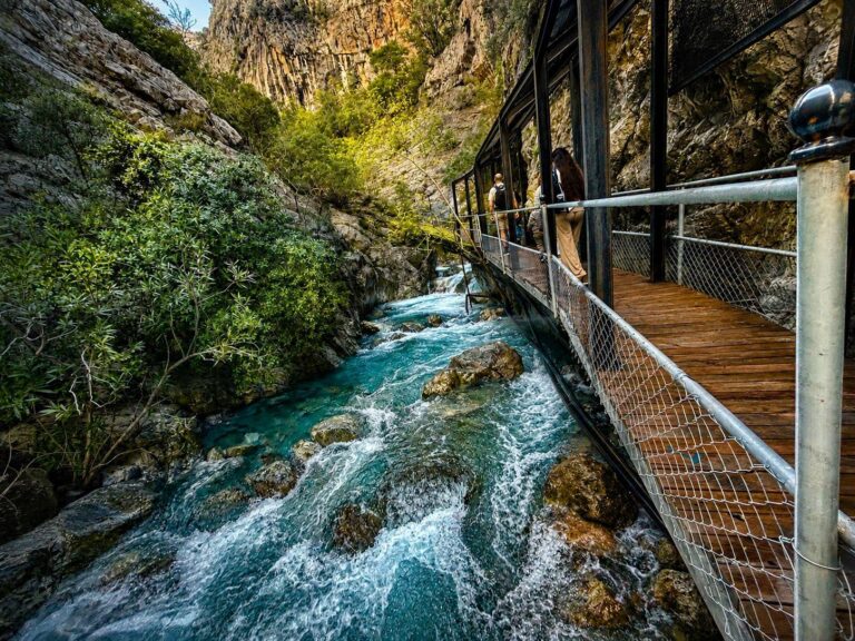 Tourists walking along the wooden boardwalk between towering limestone cliffs inside Sapadere Canyon near Alanya
