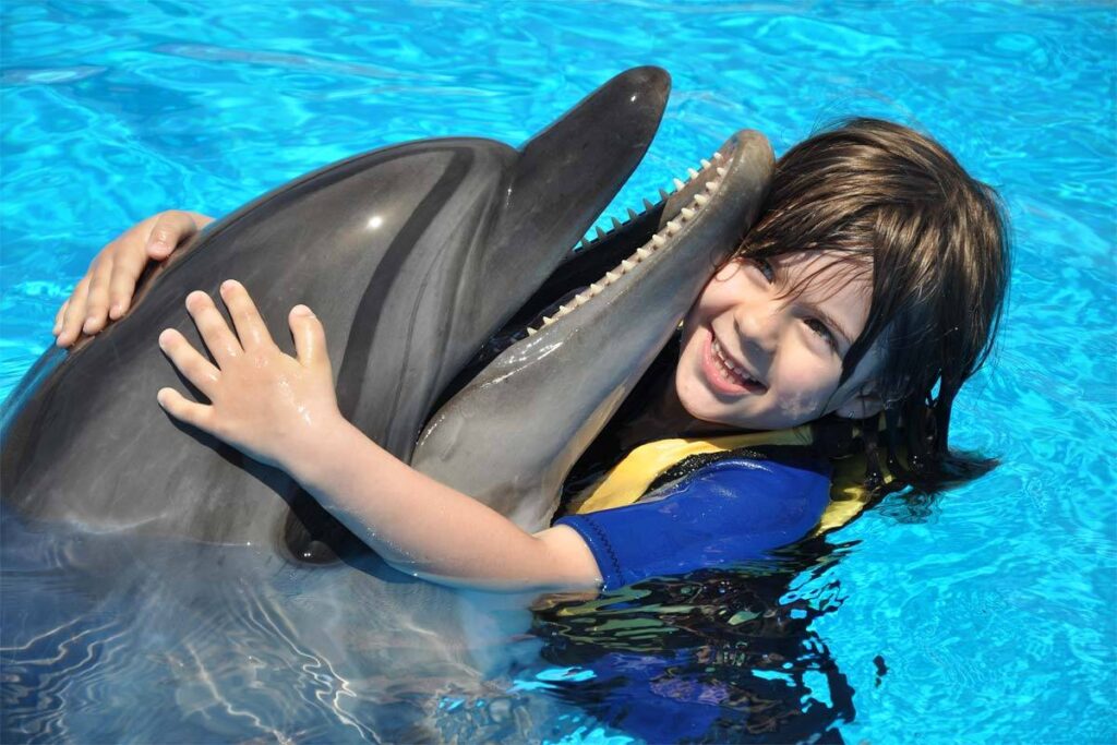 Child wearing a life jacket swimming with a bottlenose dolphin in the interaction pool at Sealanya Dolphinpark near Side, Antalya